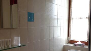 A bathroom with a toilet, sink, and glass shelf with toiletries.