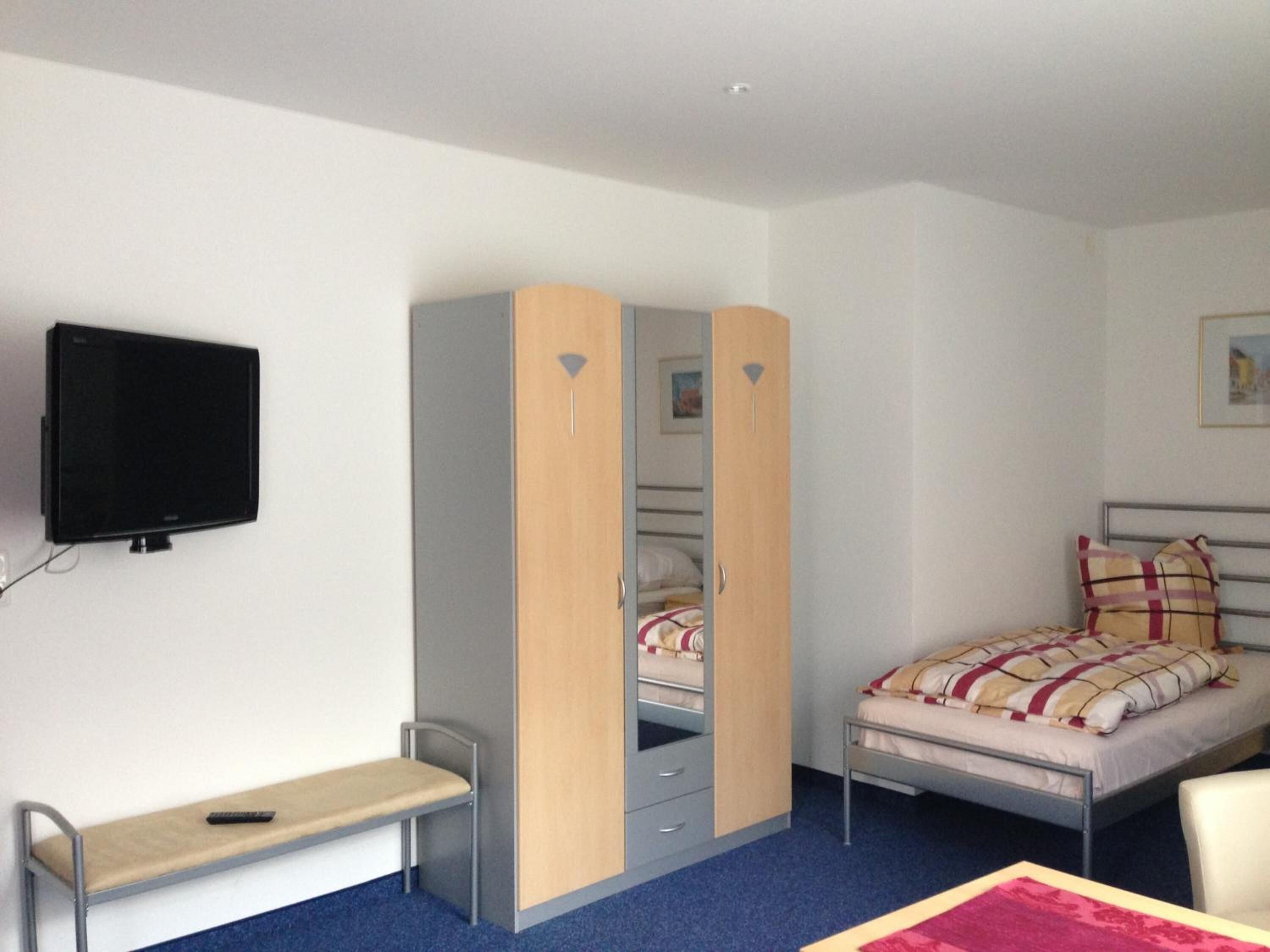 A bedroom with a bed, a desk, a wardrobe, and a television.