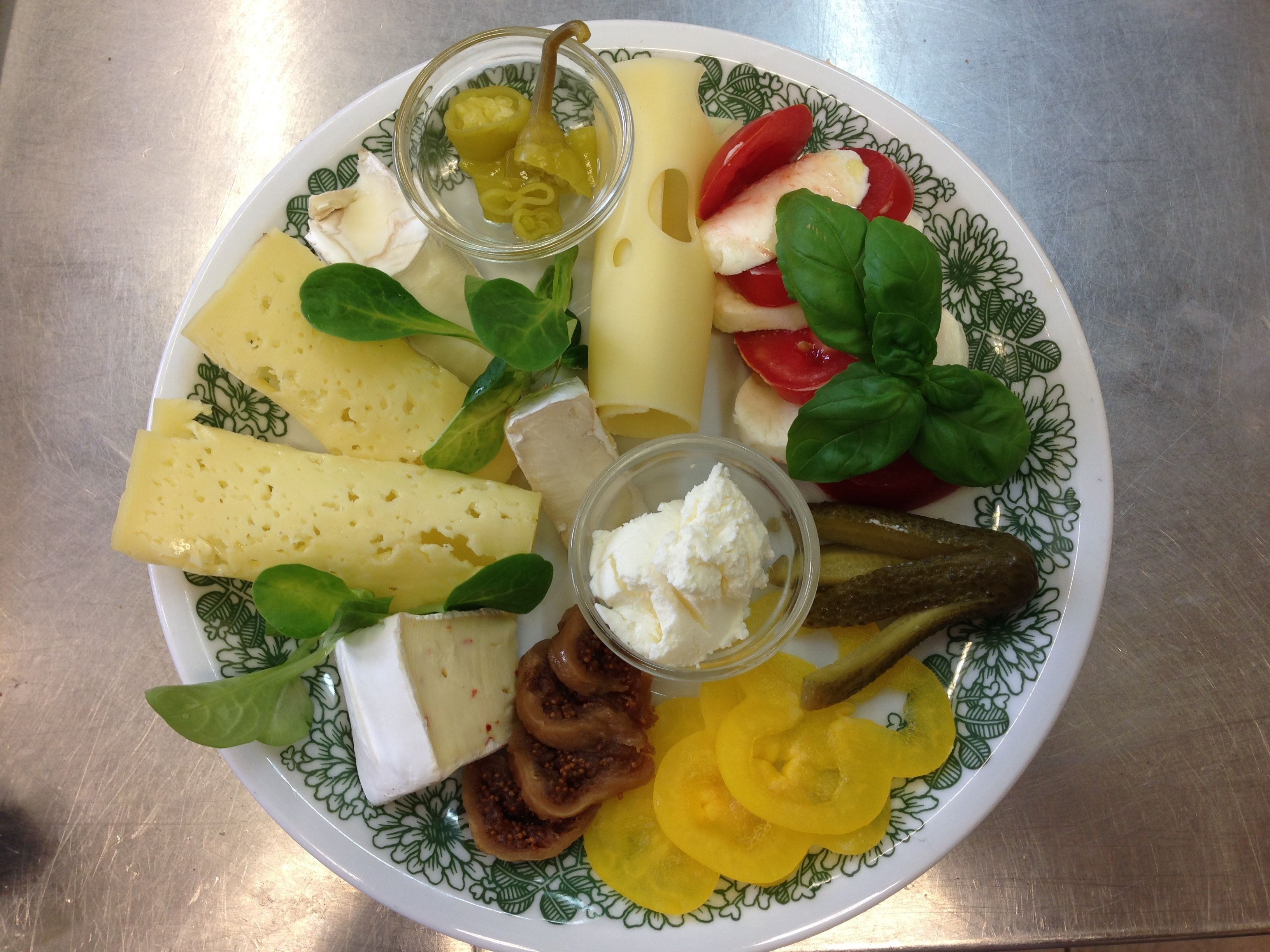 Une assiette de fromages variés, de tomates et de légumes verts.
