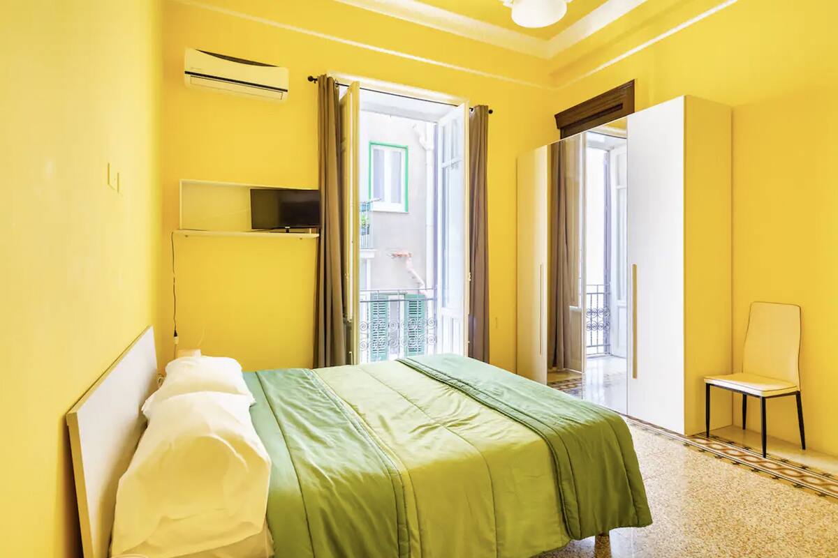 A room with a bed, a chair, and a sliding door leading to a balcony.
