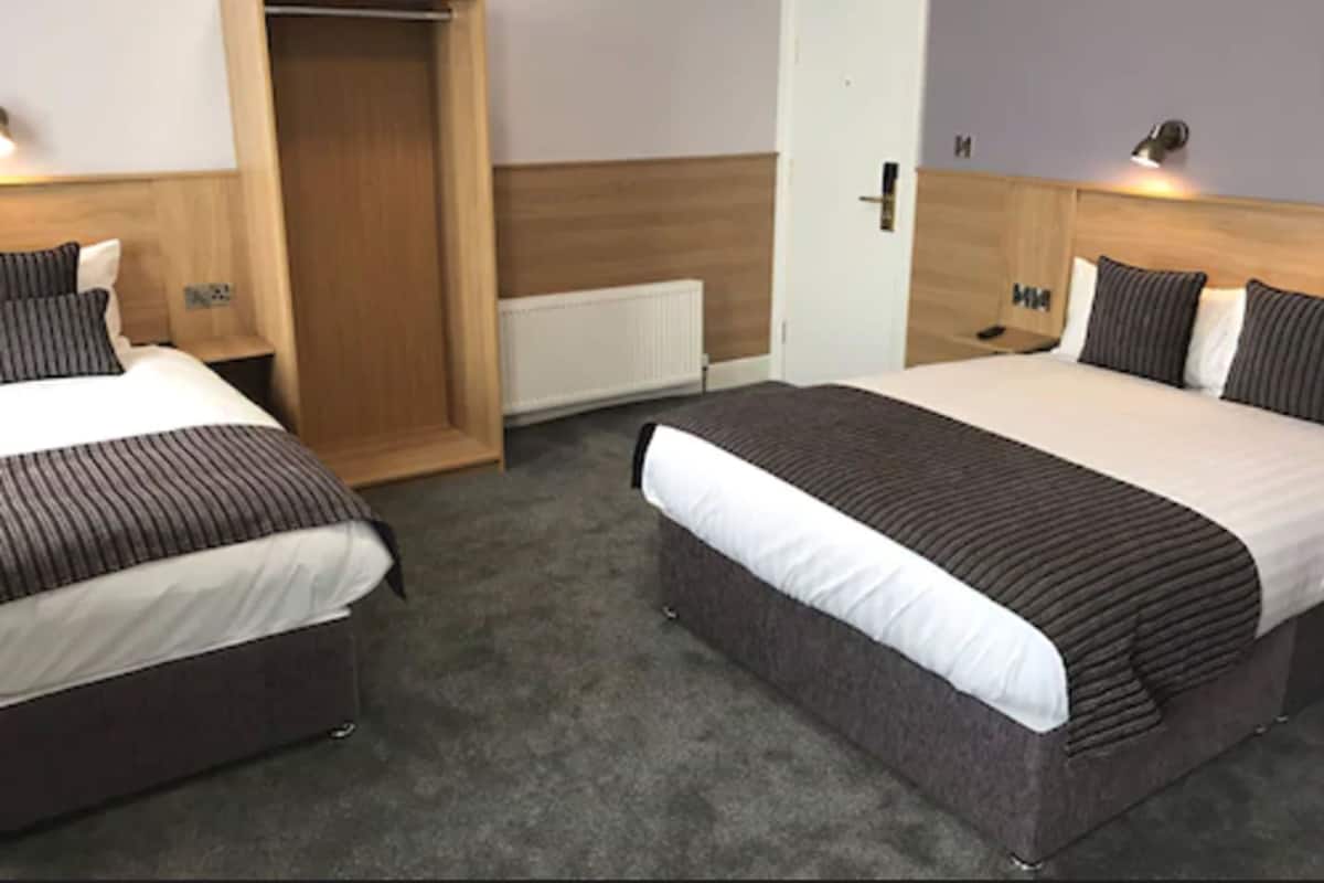 Una habitación de hotel con dos camas, un armario de madera, una puerta blanca y un radiador.