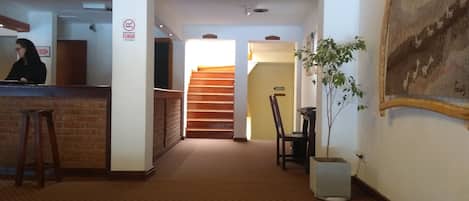 Un vestíbulo de hotel con mostrador de recepción, una escalera y una planta en maceta.