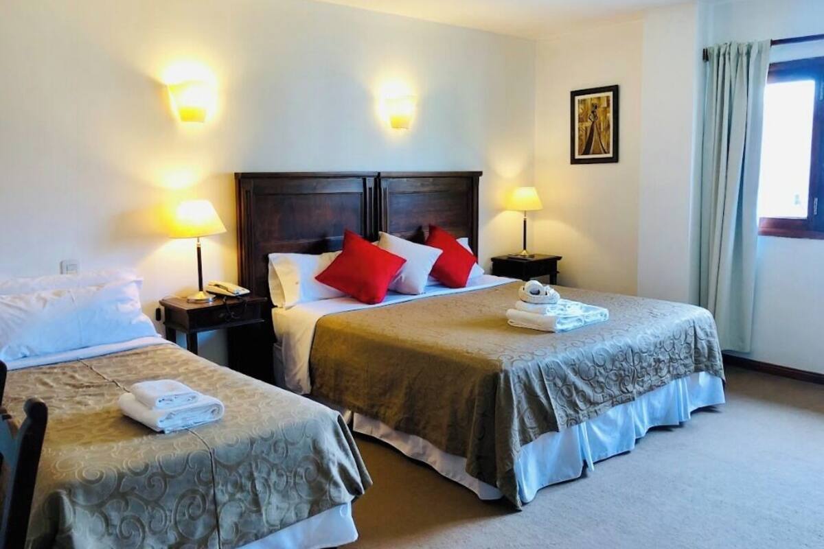 A hotel room with two beds, each with a headboard, bedside tables, lamps, and towels.