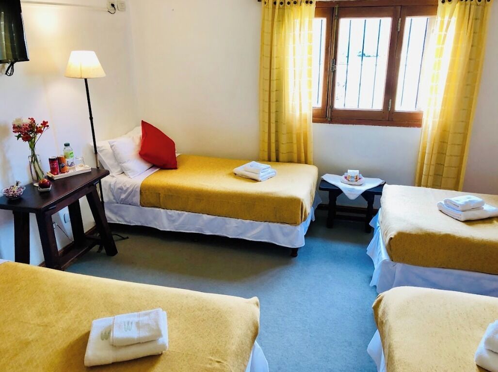 Habitación de hotel con dos camas individuales, una mesita, una lámpara y un ventanal con cortinas.