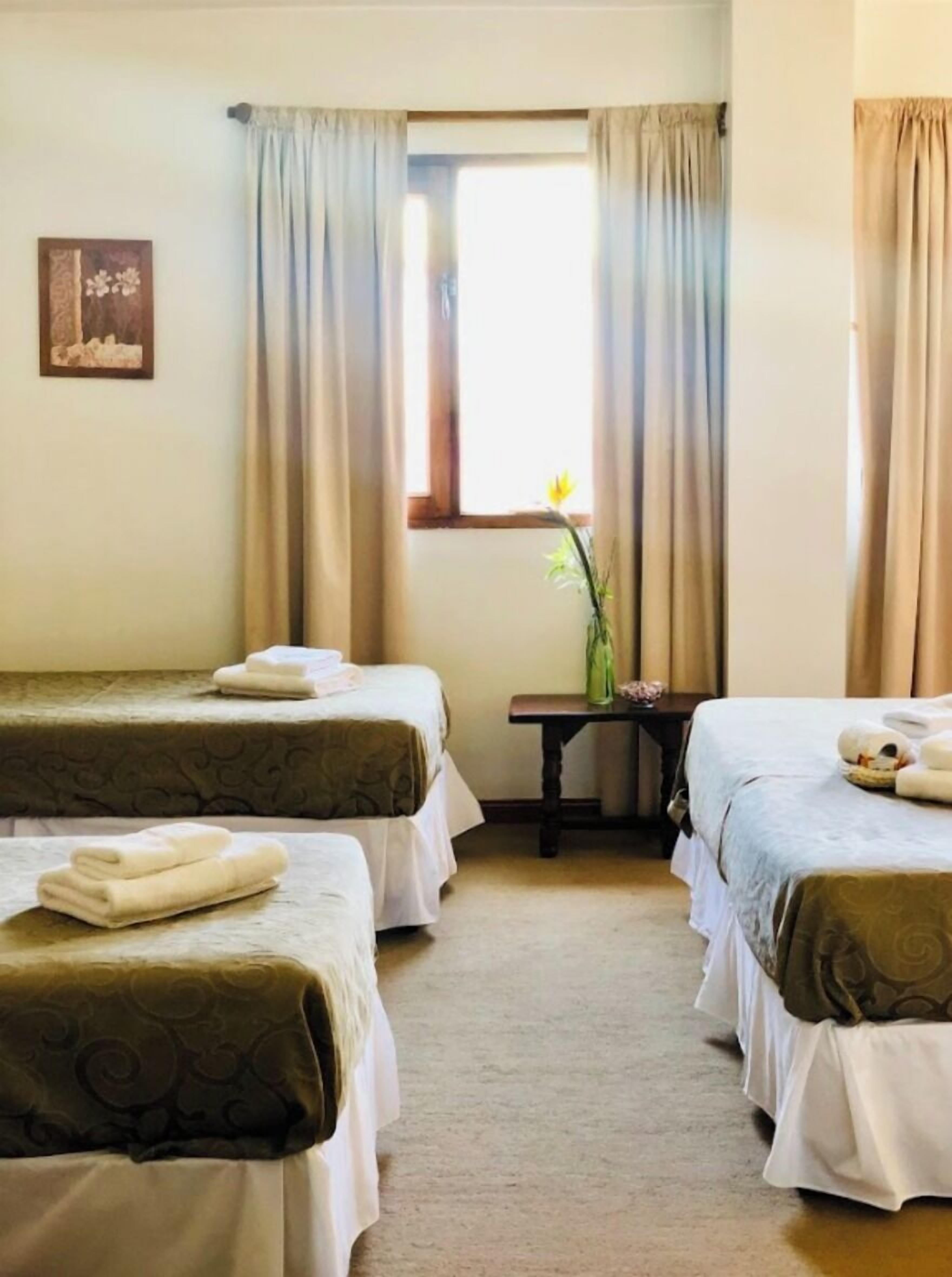 Een hotelkamer met twee eenpersoonsbedden, een tafeltje, een raam met gordijnen en een aan de muur bevestigd schilderij.