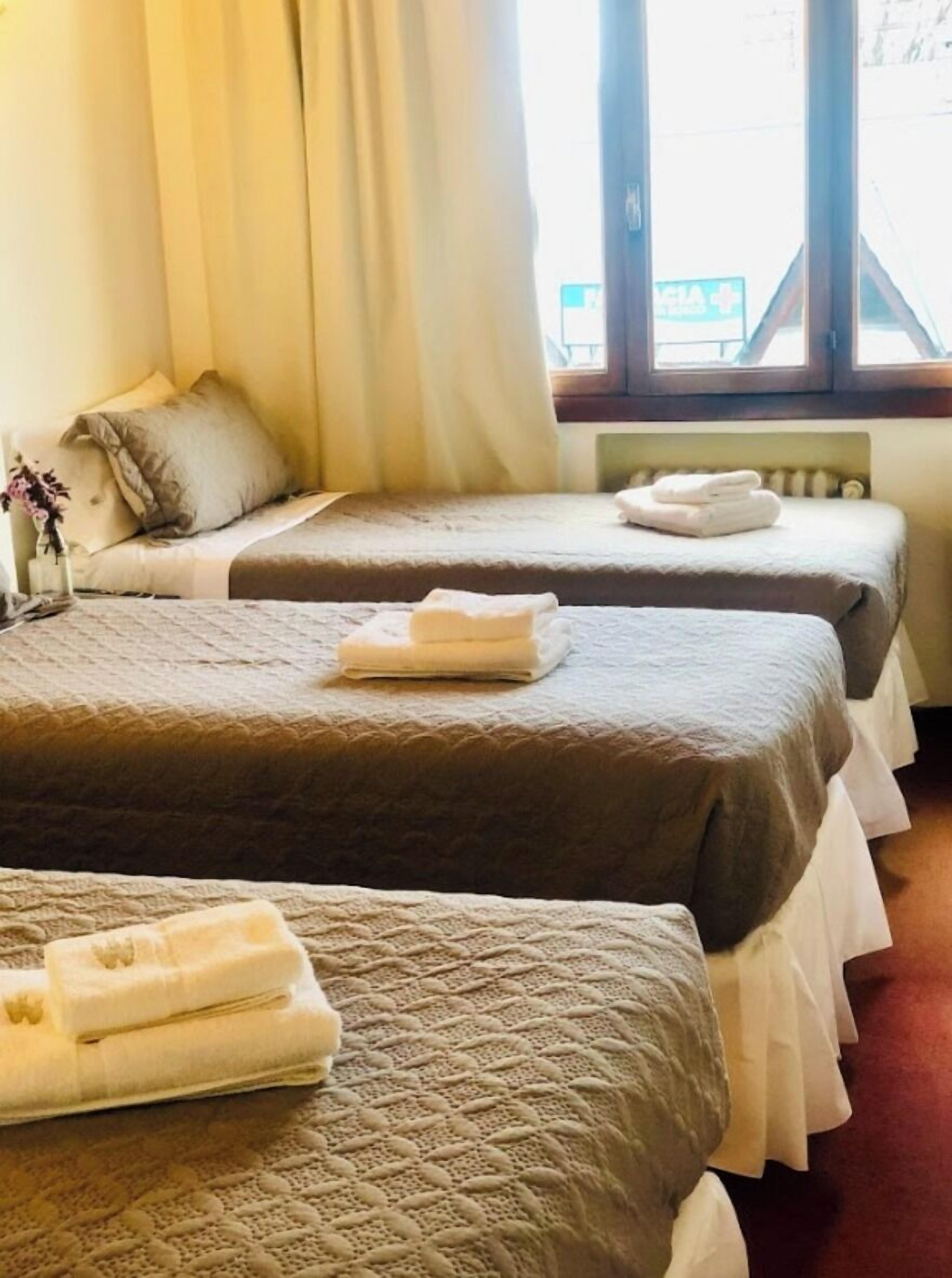 Camera d'albergo con due letti, ognuno con piumone e asciugamani piegati. Si vede una finestra con tende e un termosifone sulla parete.