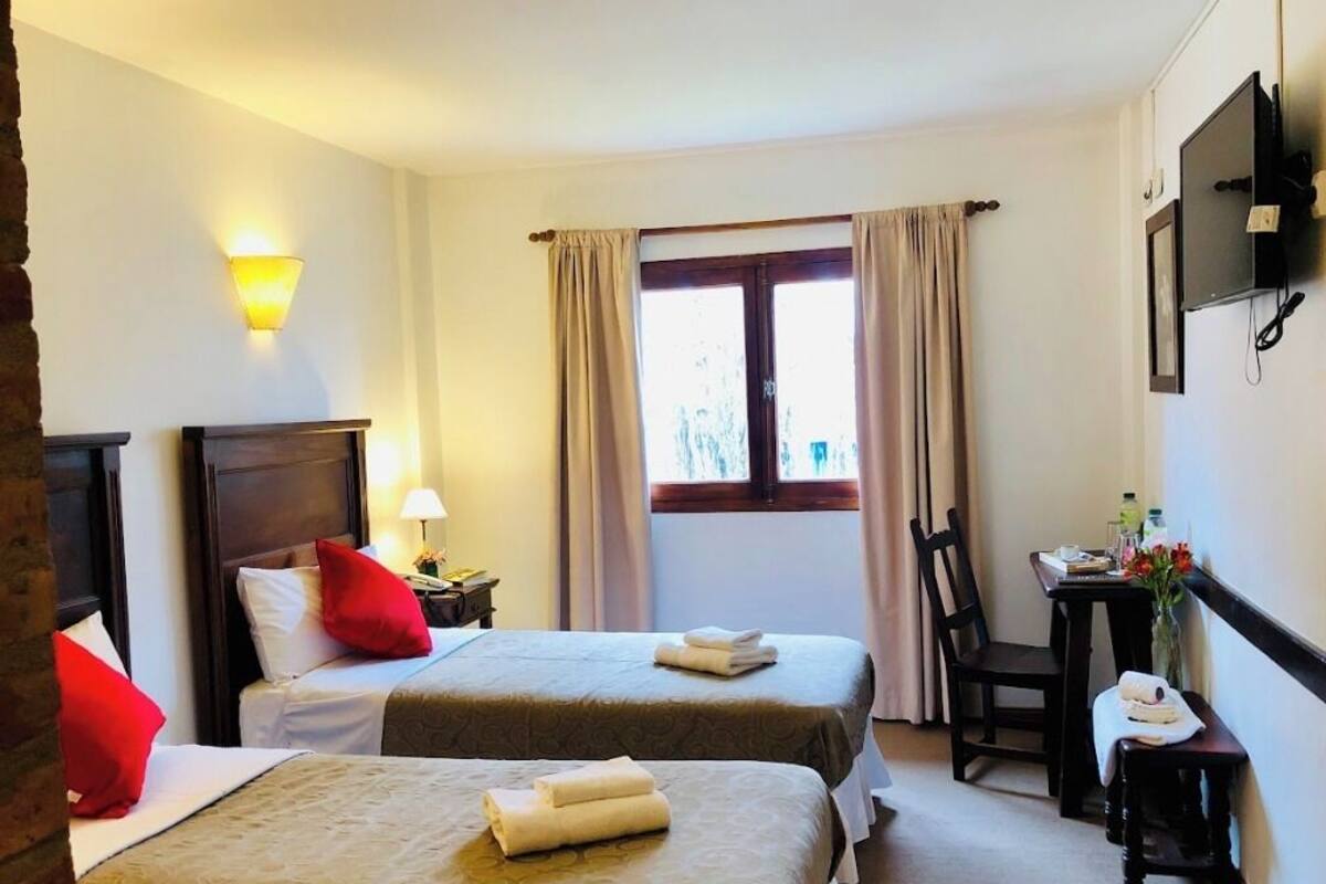 A hotel room with two beds, a desk, a chair, a TV, and a window with curtains.