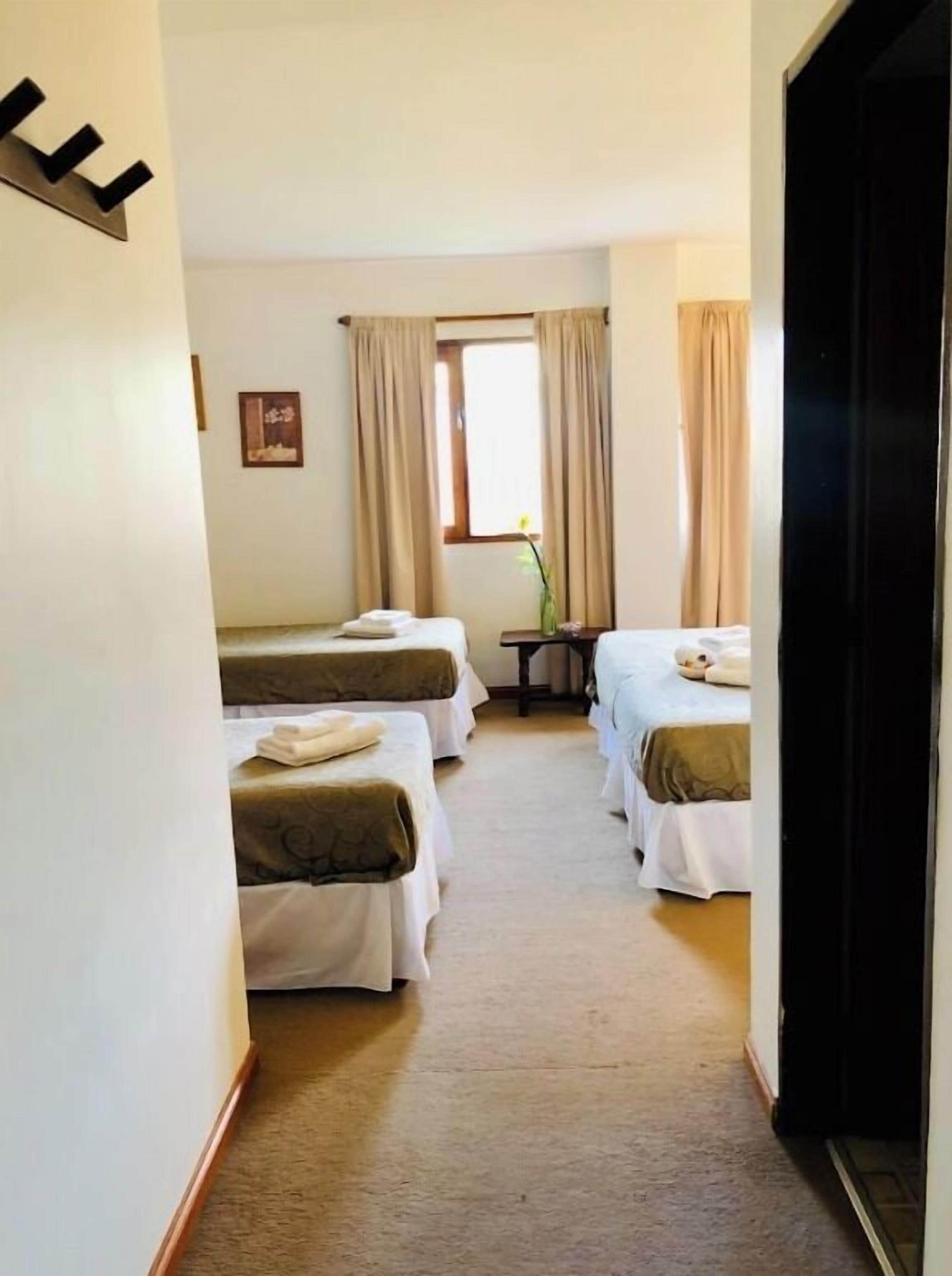 A hotel room with two beds, a small table, and a window with curtains.