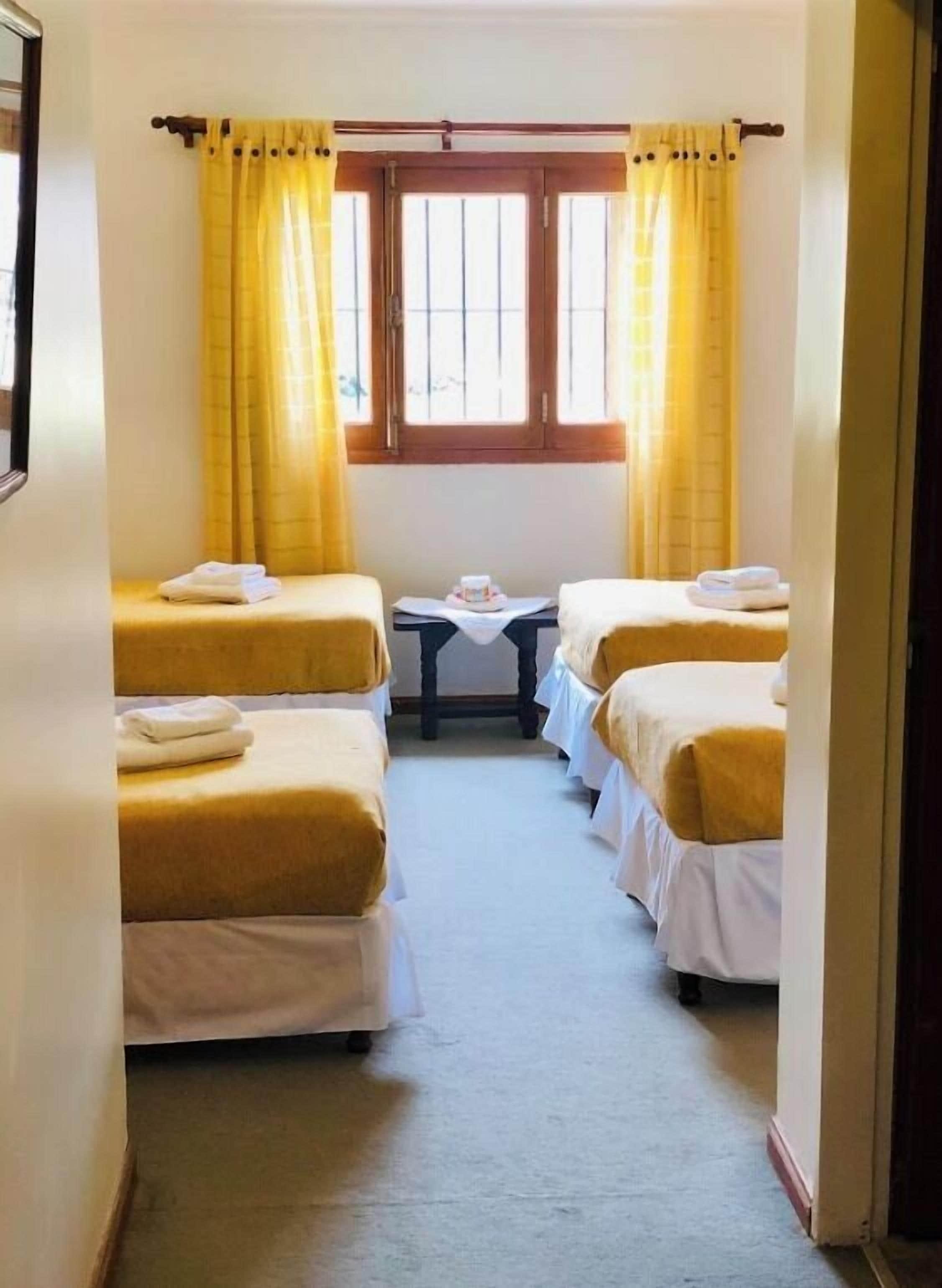 A hotel room with two beds, a small table, and a window with curtains.