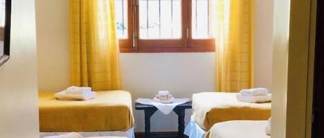 A hotel room with two beds, a small table, and a window with curtains.