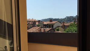 A balcony with a yellow table and two orange chairs, overlooking a residential area with terracotta roofs and greenery. - Cozy attic among the rooftops of the city (Bologna)