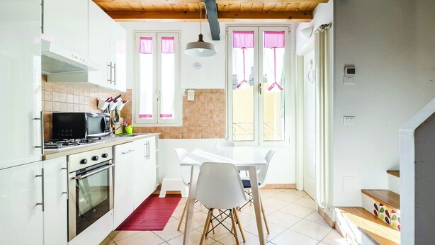 A modern kitchen with white cabinets, a gas stove, and a microwave. There is a dining area with a white table and chairs. - Cozy attic among the rooftops of the city (Bologna)