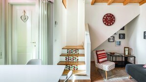 A cozy living room with a staircase, a clock, and a dining area. - Cozy attic among the rooftops of the city (Bologna)
