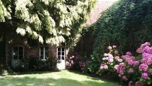 A brick house with a front door, surrounded by a well-maintained garden with hydrangea bushes and a lawn. - cottage in the park of a castle(manor) (Wierre-Au-Bois)