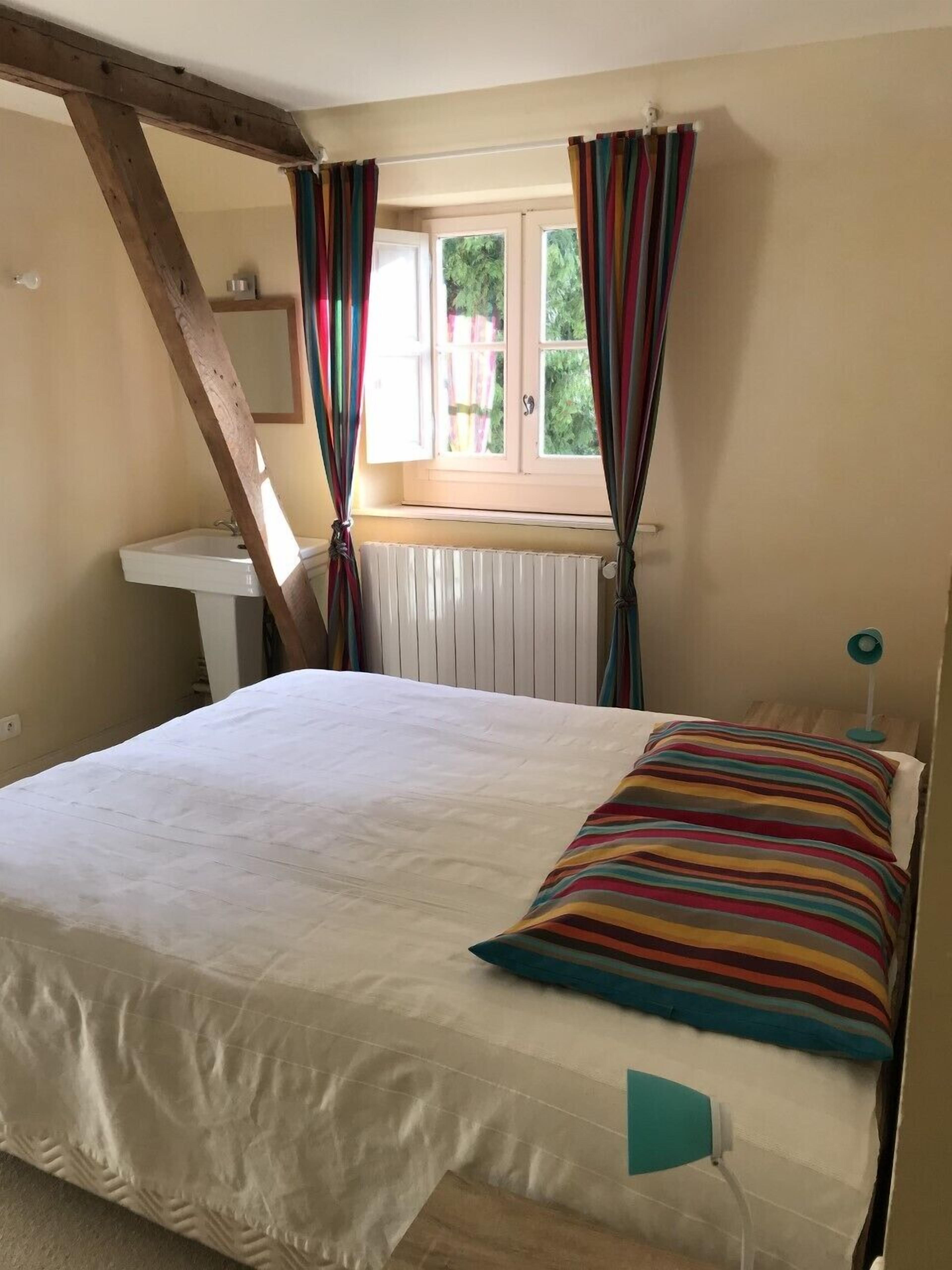 Une chambre à coucher avec un lit, une fenêtre avec des rideaux, un radiateur et une table de chevet.