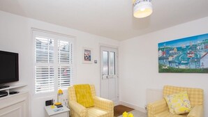 Un salon avec deux fauteuils jaunes, une table basse en bois, un téléviseur et un tableau accroché au mur.
