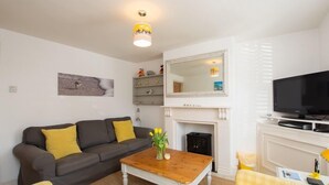 Un salon comprenant un canapé, une table basse ornée de fleurs, une cheminée, un téléviseur et une étagère sur laquelle sont disposés des objets décoratifs.