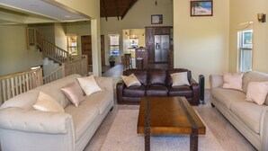 A spacious living room with a high ceiling, a brown leather sofa, a beige sofa, and a wooden coffee table.