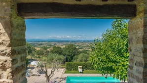 Une arche en pierre encadrant une vue sur une piscine, une végétation luxuriante et un paysage lointain.