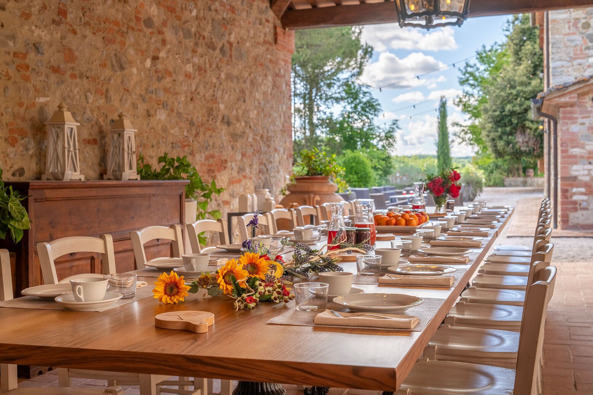 A long dining table set with chairs, a wooden table, and a view of greenery and a brick wall.