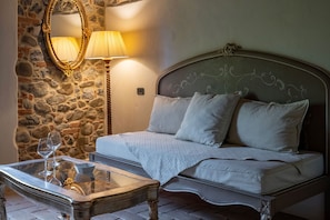 Un lit avec une tête de lit, une table de chevet avec une lampe et un miroir sur un mur en pierre.
