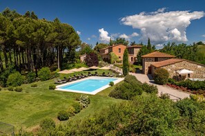 Una piscina con sillones de descanso, un edificio de piedra y un jardín con árboles.