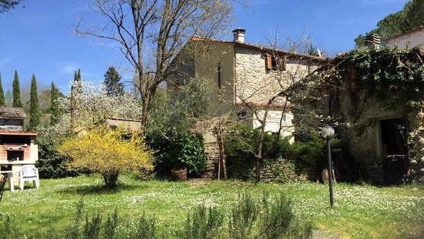 Ein Steinhaus mit Garten davor, einer kleinen Holzkonstruktion und einem strahlend blauen Himmel.