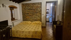Ein Schlafzimmer mit Steinswand, einem Bett mit Blumenmuster auf der Bettwäsche, einem hölzernen Schminktisch und einem Fernseher.