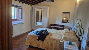 A bedroom with a bed, a nightstand, a dresser, a mirror, a radiator, and a window. - Holiday House in the beautiful  countryside ofMugello (Vicchio)