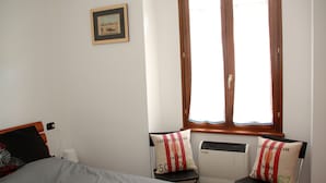 A bedroom with a bed, two chairs with cushions, a window, a radiator, and a framed picture on the wall. - Large outdoor terrace - Ground floor flat in a lovely Italian village (Dumenza)