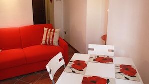 A red sofa with a cushion, a white table with four red flower placemats, and a white chair. - Large outdoor terrace - Ground floor flat in a lovely Italian village (Dumenza)