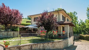A two-story house with a stone foundation, a tiled roof, and a fenced garden with potted plants. - Villa Caterina: Tuscan Villa with Private Pool near Florence and Arezzo (Pratovecchio)
