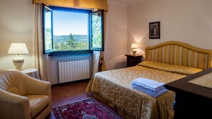 A bedroom with a bed, a chair, a window with a view, a radiator, and a lamp. - Villa Caterina: Tuscan Villa with Private Pool near Florence and Arezzo (Pratovecchio)