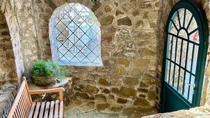 A stone-walled room with a wooden bench, a green door, and a window with a diamond pattern. - Beautiful panoramic villa in a private park with descent to the sea (Massa Lubrense)