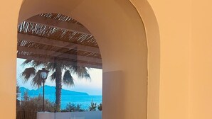 A room with a view of the sea through an arched window, a table with chairs, a book titled 'Capri Dolce Vita', and a vase with flowers. - Beautiful panoramic villa in a private park with descent to the sea (Massa Lubrense)