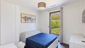 Ein Schlafzimmer mit einem Bett, einem Gemälde, einem Fenster und einer Tür, die auf einen Balkon führt.