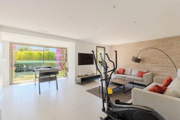 A modern living room with a treadmill, a sofa, a coffee table, and a TV. - 5* villa with private pool on prestigious estate (Villeneuve-Loubet)
