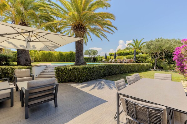 Um pátio externo com piscina, espreguiçadeiras e guarda-sóis.