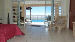 Una habitación con cama, una silla, una piscina y vistas al mar.