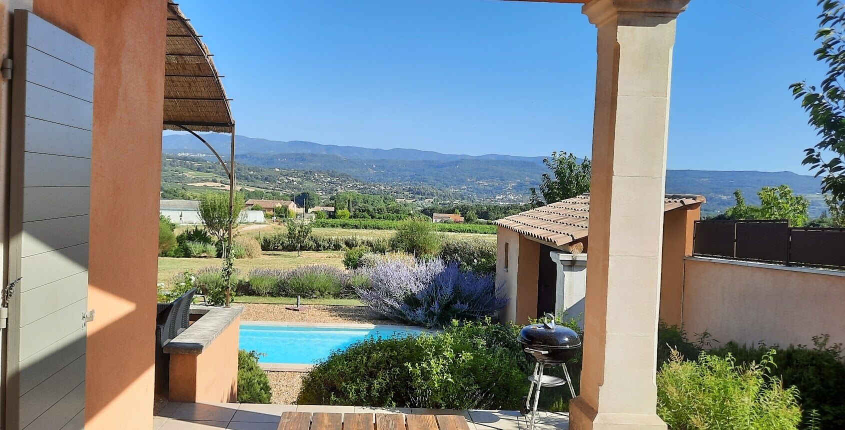 Um pátio com piscina, churrasqueira e vista para um vale com casas e montanhas.