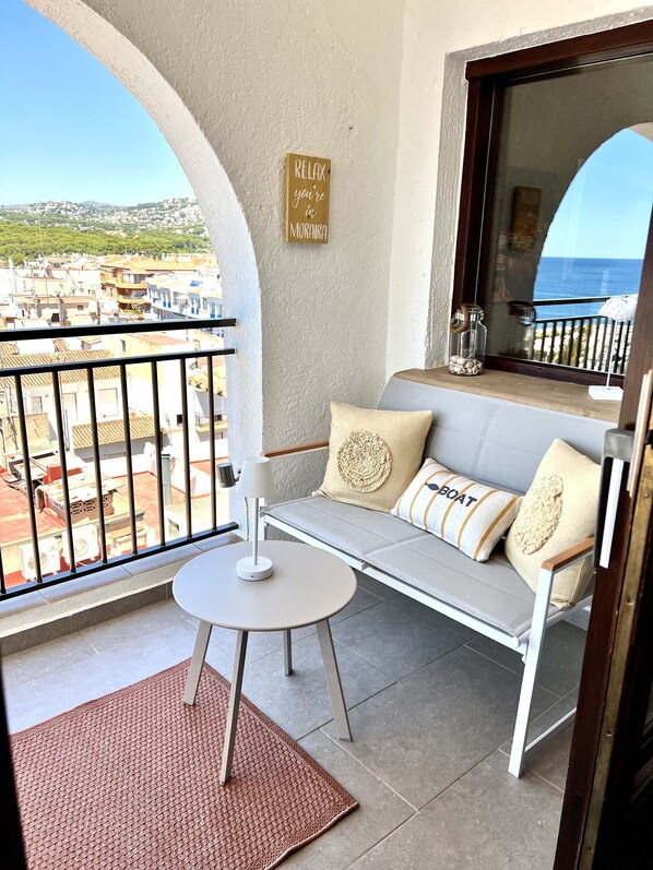 Un balcon avec un canapé blanc, une petite table et une vue sur une ville côtière.