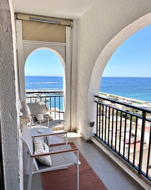 Un balcon avec des chaises blanches et une table, donnant sur une marina et la mer.