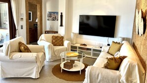 Een moderne woonkamer met een flatscreen televisie, twee witte fauteuils, een bank, een salontafel en een tv-meubel.