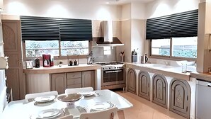 Una cocina moderna con comedor, que cuenta con estufa, horno y ventanas amplias con persianas.