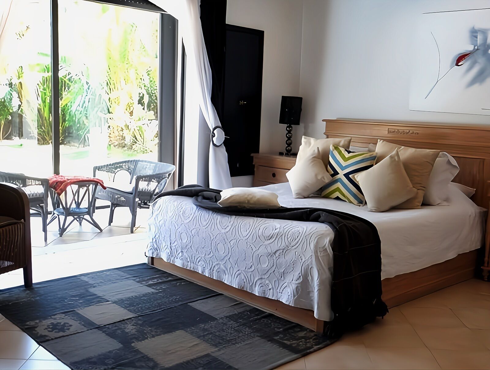 A bedroom with a bed, a nightstand, a lamp, and a view of the outdoors.