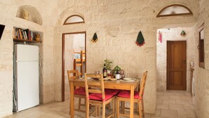 Una habitación con paredes de piedra, una mesa de comedor de madera, sillas y un refrigerador blanco.
