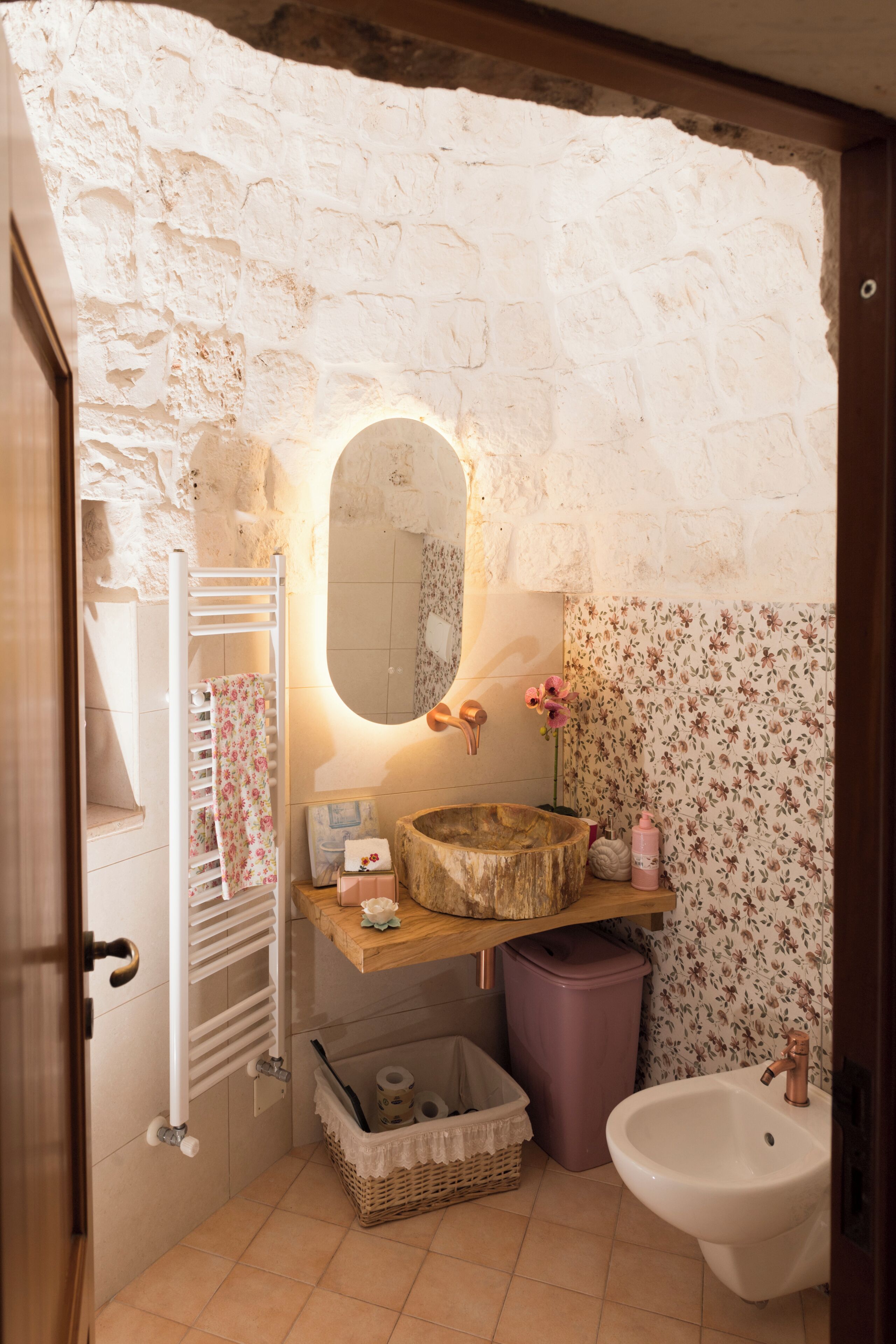 Un baño con pared de piedra, tocador de madera, lavabo blanco y espejo.