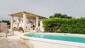 Una piscina con pérgola, edificio de piedra y plantas en macetas.
