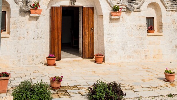 Un edificio de piedra tradicional con una puerta de madera central, varias ventanas y macetas con plantas.