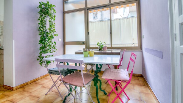 Un comedor con una mesa blanca, dos sillas rosadas y una planta verde en la pared.